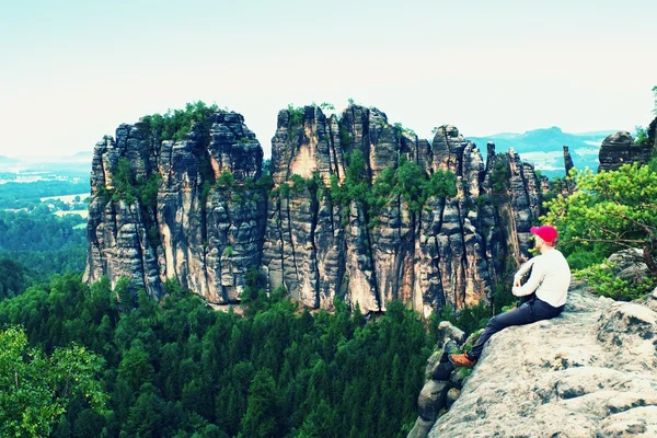 Высокий человек в красной бейсболке сидит на скале и смотрит в горы. Тёмный силуэт скал . — стоковое фото