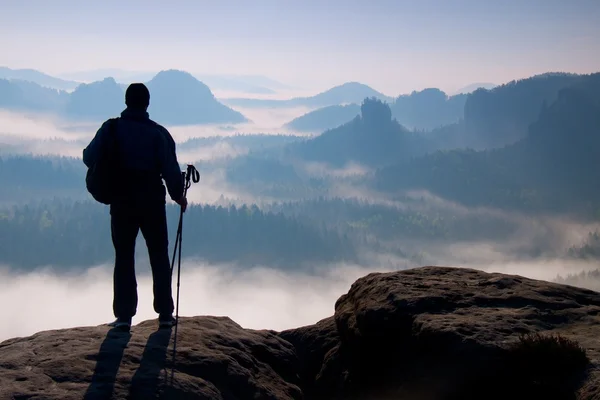 Silhouette scura di escursionista con bastoni in mano. Sunny alba di primavera in montagne rocciose. Escursionista con zaino sportivo in piedi sulla cima rocciosa sopra la valle . Fotografia Stock
