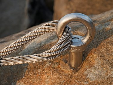 Çelik cıvata çapa göz kaya ayrıntı. Çelik halat bitiş düğüm. Via ferrata kaya dağcılar yolunda. Demir blok içinde sabit ip bükülmüş.