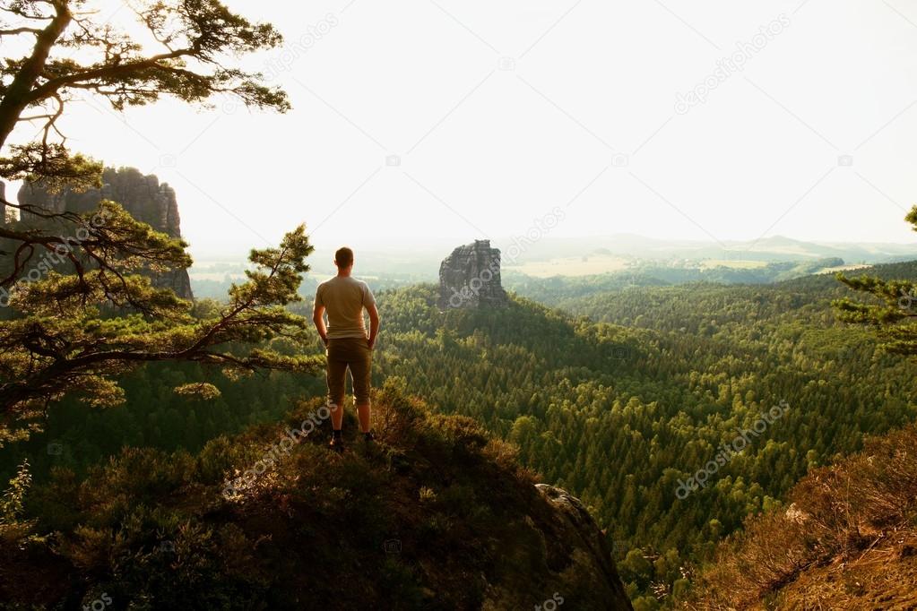 Tall tourist climbing on sharp cliff and  overlooking beautiful view above forest valley bellow.