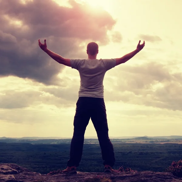 Gesture of triumph. Happy hiker in greyshirt and dark trousars. Tall man on the peak of sandstone cliff watching down to landscape. — Stock Photo, Image