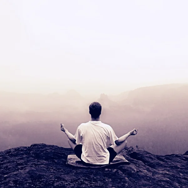 L'uomo sta facendo posa Yoga sulle rocce picco entro la mattina nebbiosa — Foto Stock