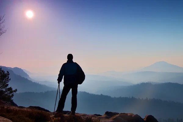 Silhouette de touriste avec poteaux à la main. Randonneur avec sac à dos sportif debout sur le point de vue rocheux au-dessus de la vallée brumeuse. Matin ensoleillé dans les montagnes rocheuses . — Photo