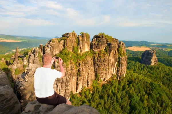 Uçurum rock ve alır fotoğraf peyzaj feryat akıllı telefon kısa saçlı adam. Güneşli bir günde rocky Dağları — Stok fotoğraf