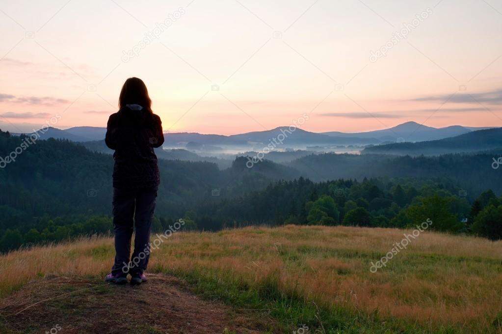 Long hair woman stand on meadow with golden stalks of grass and waiting for sunrise