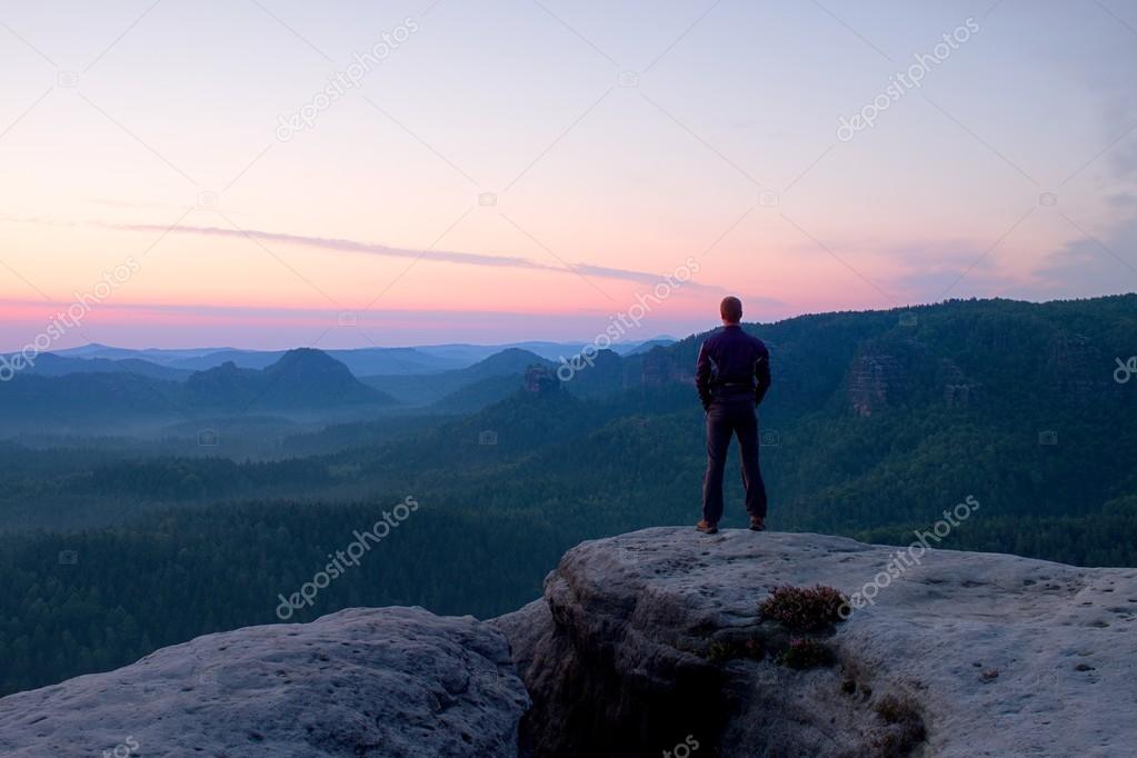 Hiker stand on the cliff of sandstone rock empire and watch over the misty and foggy morning valley