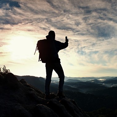 Turist ağır sırt çantası ile akıllı telefon ile fotoğraf çeker. Adam kayalık tepe üzerinde. Rüya gibi adamlara Vadisi aşağıdaki