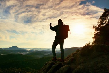 Turist ağır sırt çantası ile akıllı telefon ile fotoğraf çeker. Adam kayalık tepe üzerinde. Rüya gibi adamlara Vadisi aşağıdaki