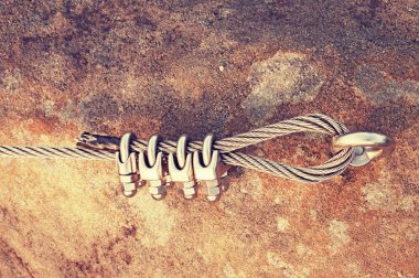 Solid knot on steel rope. Iron twisted rope fixed in block by screws snap hooks. Detail of rope end anchored into sandstone rock clipart