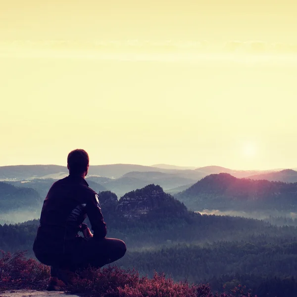 Sunrise spor. Heather çalılar, çömelme bir konumda bir kayanın üzerinde karanlık eşofman içinde uzun yürüyüşe çıkan kimse içinde zevk sahne