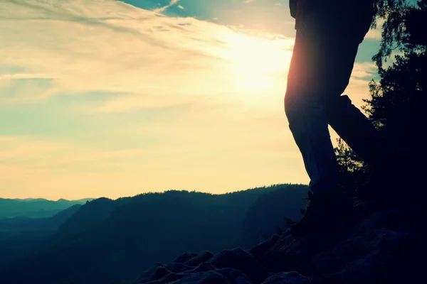 Woman hiker legs in tourist boots stand on mountain rocky peak. Sun n background — Stock Photo, Image