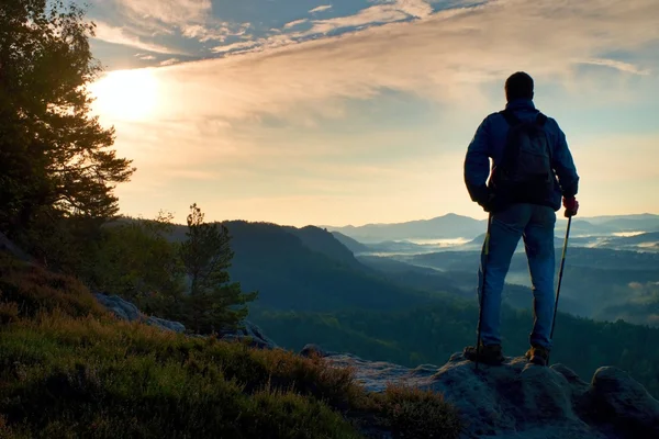 Silhouet van toeristische met rugzak. Zonnige voorjaar daybreak in rocky mountains. Wandelaar met sportieve rugzak staan op rotsachtige oogpunt boven mistige vallei. — Stockfoto