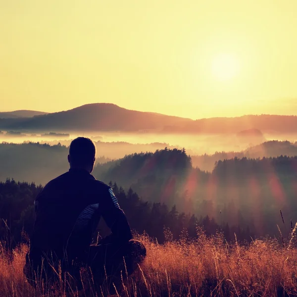 Hiker in squatting position in high grass meadow  enjoy the colorful sunrise scenery — Stock Fotó