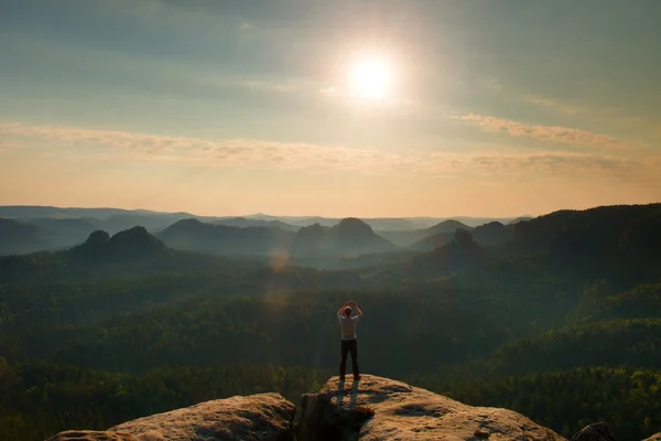 Man neemt foto's met slimme telefoon op Top van rock rijk. Dromerige fogy landschap, voorjaar oranje roze mistige sunrise in een prachtige vallei van Saksen Zwitserland park. — Stockfoto