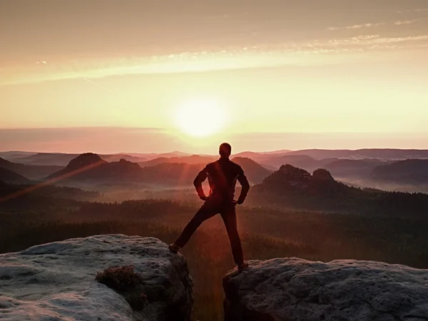 跳跃在黑色的徒步旅行者庆祝胜利之间两个多岩石的山峰。美好的黎明，与头顶的太阳.. — 图库照片