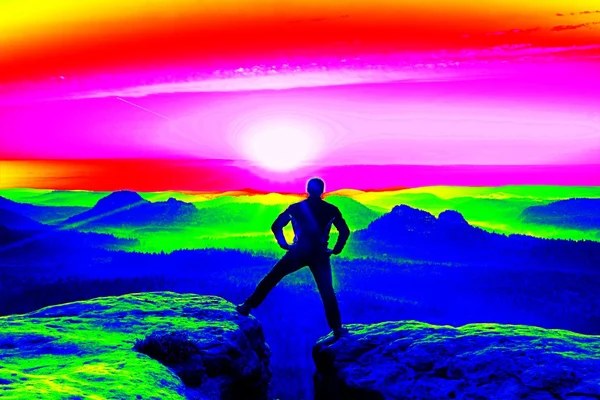 Fantastiska infraröd skanning. Tall vandrare i svart på den steniga toppen. Underbar gryning i bergen, tunga orange dimma i djupa valle — Stockfoto