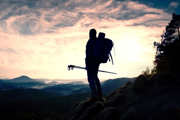 Туристичний гід з полюсом в руці. Ведучий зі спортивним рюкзаком стоїть на скелястій точці над туманною долиною. Сонячний весняний ранковий день — стокове фото