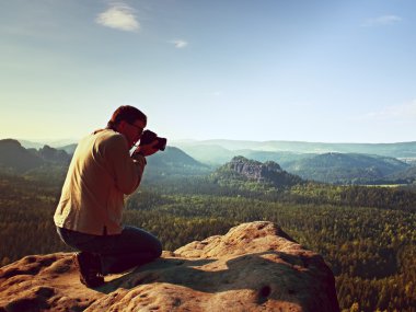 Siyah saçlı adam fotoğraf büyük ayna kamera dağ tepe üzerinde boynundaki güneş doğarken alıyor.
