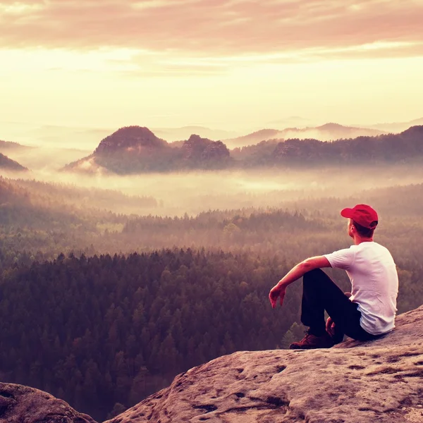 Yetişkin sporcu beyaz gömlek, karanlık trousars ve kırmızı kap. Zencefil kısa saçlı adam keskin uçurum rocky Dağları Park vadi üzerinde oturmak