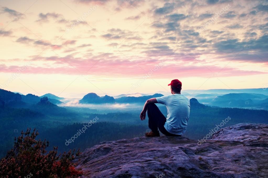 Deportista adulto en camisa blanca, pantalones oscuros y gorra roja. jengibre hombre de pelo corto sentarse en el acantilado agudo sobre el valle en las montañas rocosas parque — Foto de Stock
