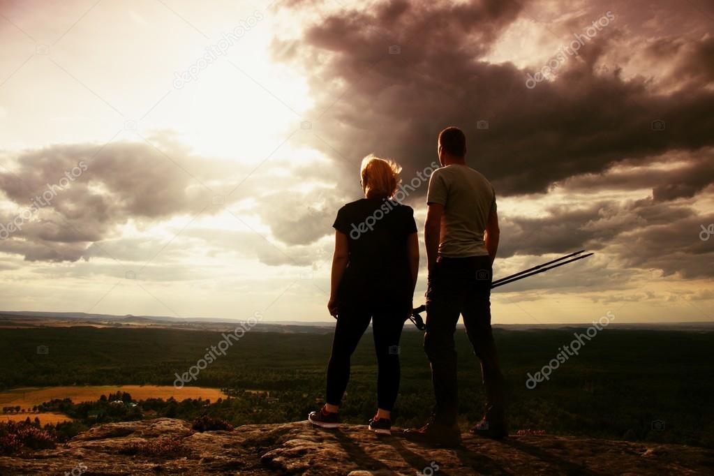 Couple enjoying marvellous moments during sunset . Young pair of hikers on the peak of rock watch over valley to Sun.