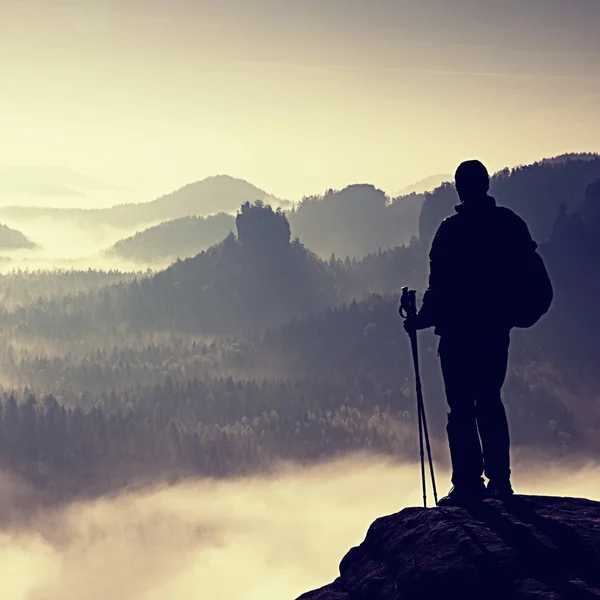 Dark silhouette of hiker with poles in hand. Sunny spring daybreak in rocky mountains. Hiker with sporty backpack stand on rocky peak  above valley. — Stock Photo, Image