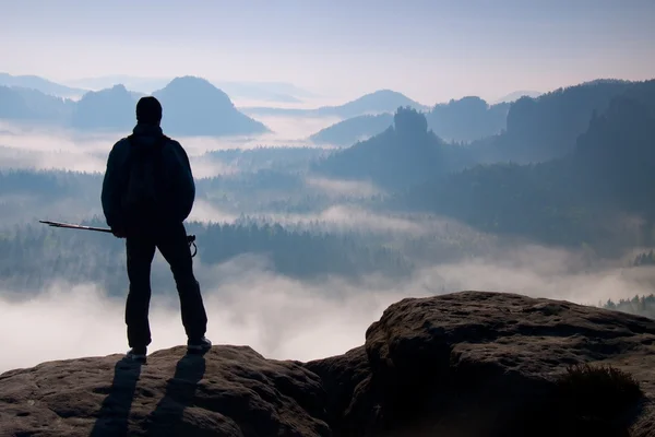 在洛矶山脉有雾的日子。旅游与剪影手杆。徒步旅行者站在岩石看法点上方迷雾笼罩的山谷. — 图库照片