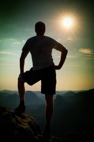 Sportler in Hemd und Hose. Mann steht auf dem Gipfel der Sandsteinklippe im Park der Felsenimperien und blickt ins neblige Tal. — Stockfoto