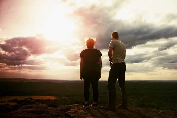 Pareja disfrutando de maravillosos momentos durante el atardecer. Un joven par de excursionistas en el pico de la roca vigilan el valle hasta el Sol . — Foto de Stock