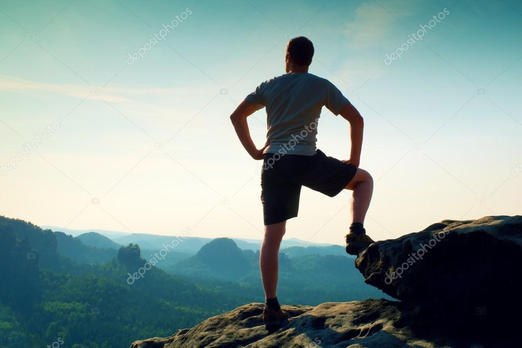 Sportsman in shirt and pants. Man is standing on the peak of sandstone cliff in rock empires park and watching  into misty valley.