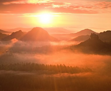 Marvelous red awakening. Autumn beautiful valley. Peaks of hills are sticking out from fog red and orange  Sun rays. clipart