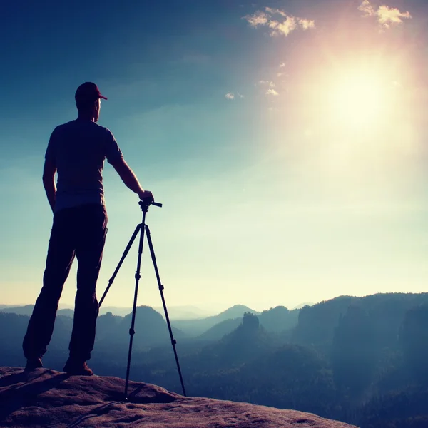 Professionelle Fotograf bleiben mit Stativ auf Klippe und Denken. verträumte Nebellandschaft, blauer nebliger Sonnenaufgang in einem wunderschönen Tal unten — Stockfoto