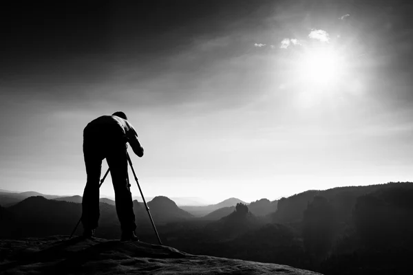 Appassionato di fotografia soggiorno con treppiede sulla scogliera e pensare. Paesaggio nebbioso da sogno, alba nebbiosa blu in una bellissima valle sottostante — Foto Stock