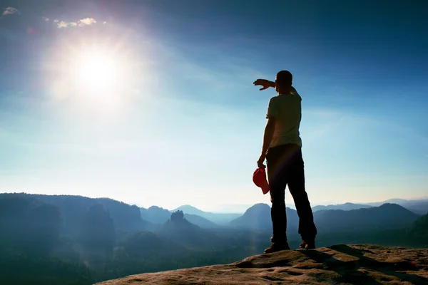 Hiker in red cap on peak of rock in rock empires park and watching over the misty and foggy morning valley to Sun. Beautiful  trip. — Stock Photo, Image