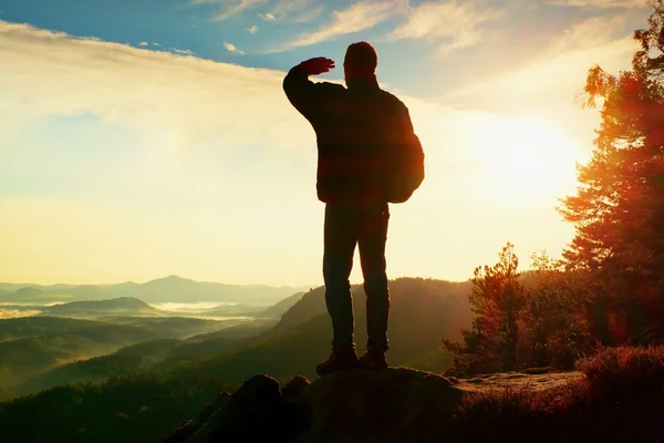 Silhouette di turista con zaino. Sunny alba di primavera in montagne rocciose. Escursionista con zaino sportivo in piedi sul punto di vista roccioso sopra la valle nebbiosa . — Foto Stock