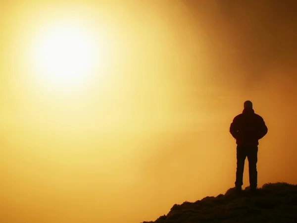 Tall adult hiker in black on the peak of the world . Heavy orange mist bellow in valley. Wonderful daybreak in mountains. — Stock Photo, Image