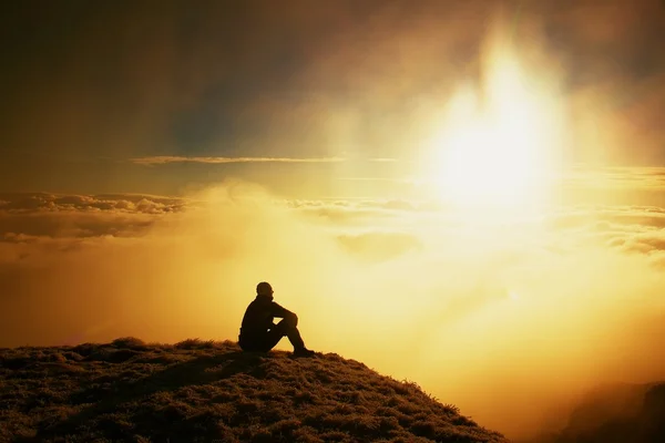 Großer erwachsener Wanderer in schwarz auf dem Gipfel der Welt. Schwerer orangefarbener Nebel liegt im Tal. wunderbarer Tagesaufbruch in den Bergen. — Stockfoto