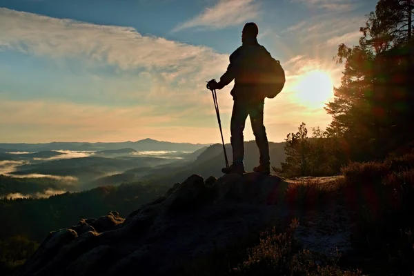 Silueta de excursionista solo con bastones en la mano. Turista con mochila deportiva de pie en el punto de vista rocoso por encima del valle brumoso. Amanecer soleado de primavera en montañas rocosas . —  Fotos de Stock