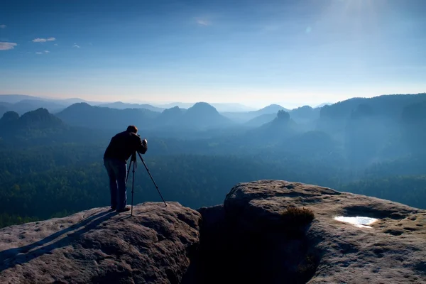 Professional on cliff. Nature photographer takes photos with mirror camera on peak of rock. Dreamy blue fogy landscape, — Stock Photo, Image