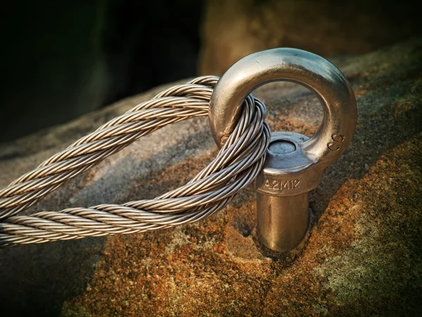 Çelik cıvata çapa göz kaya ayrıntı. Çelik halat bitiş düğüm. Via ferrata kaya dağcılar yolunda. Demir blok içinde sabit ip bükülmüş.
