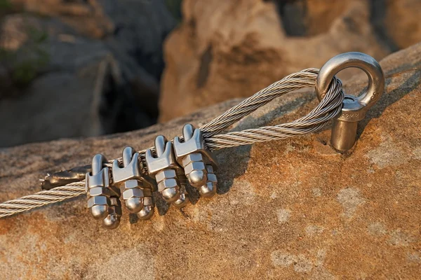 Solid knot on steel rope. Iron twisted rope fixed in block by screws snap hooks. Detail of rope end anchored into sandstone rock — Stock Photo, Image