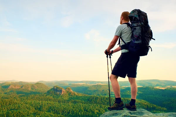 Tall backpacker med stolpar i handen. Solig sommar evenng i Klippiga bergen. Vandrare med stor ryggsäck stå på rocky utsiktsplats över dalen. — Stockfoto