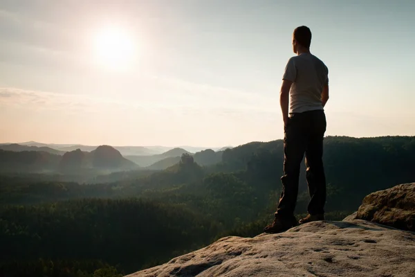 Satisfaire grand randonneur en chemise grise et pantalon foncé. Sprtsman sur le pic du bord de roche pointu regardant vers le bas au paysage . — Photo