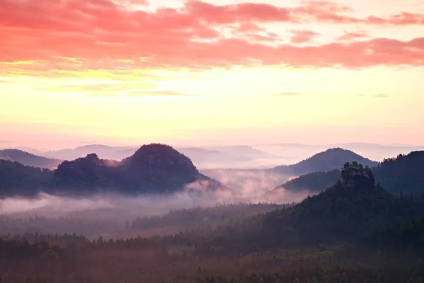 Amanhecer vermelho. Amanhecer enevoado numa bela colina. Picos de colinas estão saindo do fundo nebuloso, o nevoeiro é vermelho e laranja devido aos raios solares . — Fotografia de Stock