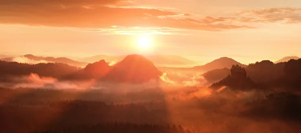 Amanecer brumoso rojo en una hermosa colina. Los picos de colinas sobresalen del fondo brumoso, la niebla roja y naranja debajo de los rayos del sol . — Foto de Stock