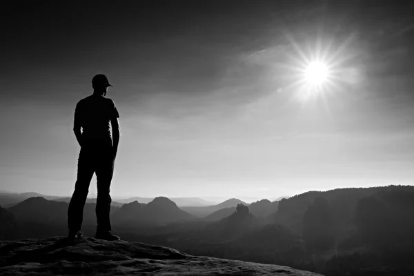 Alone man in red cap on peak of sharp peak in rock empires park and watching over the misty and foggy morning valley to Sun. Beautiful moment — Stock Photo, Image