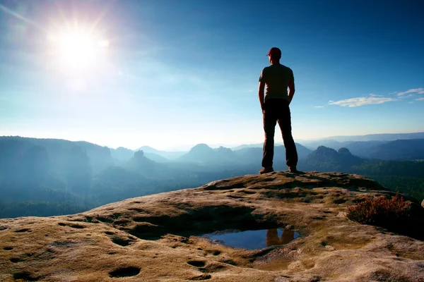 Hombre solo en gorra roja en el pico del pico agudo en el parque de imperios rocosos y vigilando el brumoso y brumoso valle matutino hasta el Sol. Hermoso momento — Foto de Stock