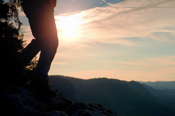 Mujer piernas excursionistas en botas turísticas de pie en la montaña rocosa pico. Sol n fondo —  Fotos de Stock