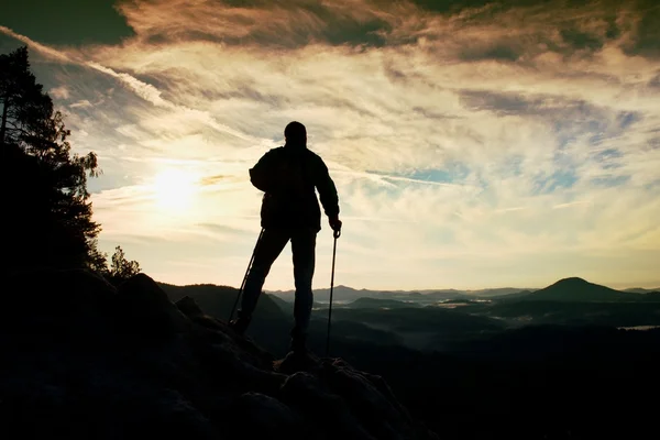 Силуэт одинокого туриста с шестом в руке. Турист со спортивным рюкзаком стоит на скалистом месте над туманной долиной. Солнечный весенний рассвет в скалистых горах . — стоковое фото