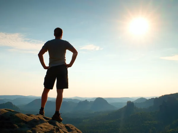 Ein glücklicher Wanderer steht auf einer steilen Klippe im Park der Felsenimperien und blickt über das neblige Morgental zur Sonne. — Stockfoto